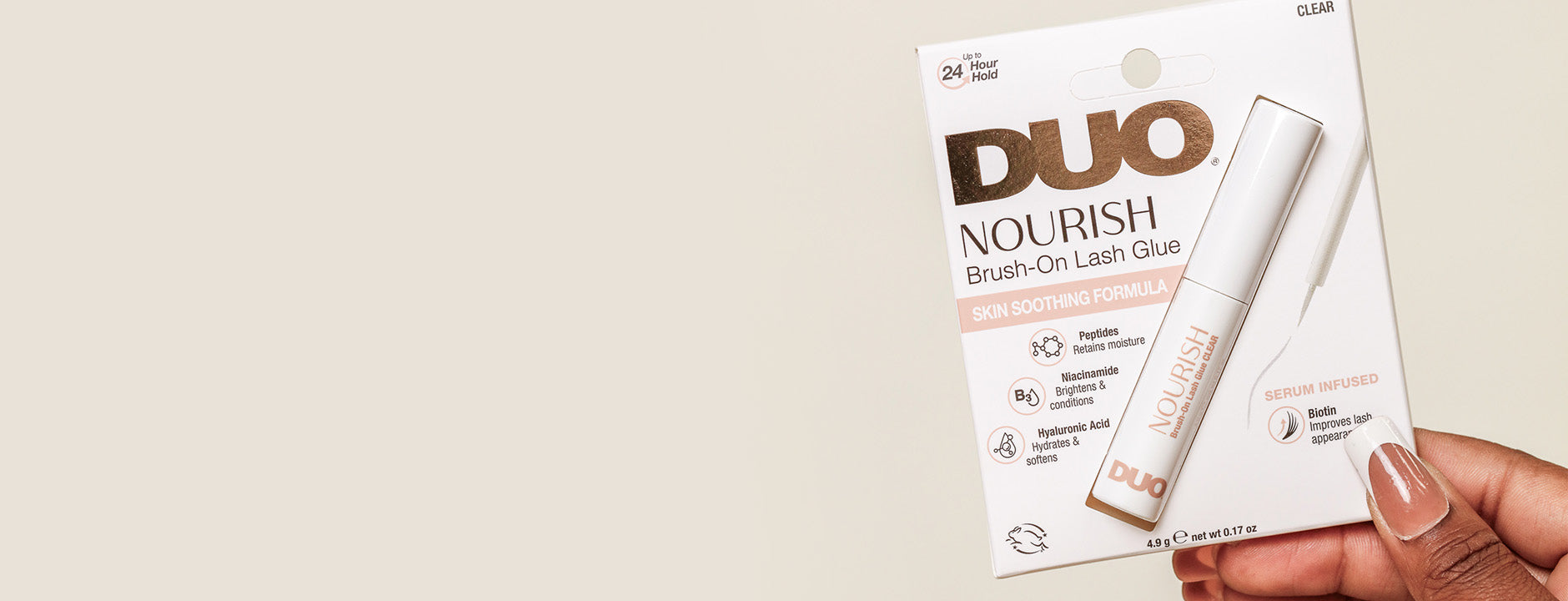 DUO Nourish Brush-On Lash Glue packaging held by a hand on a beige background
