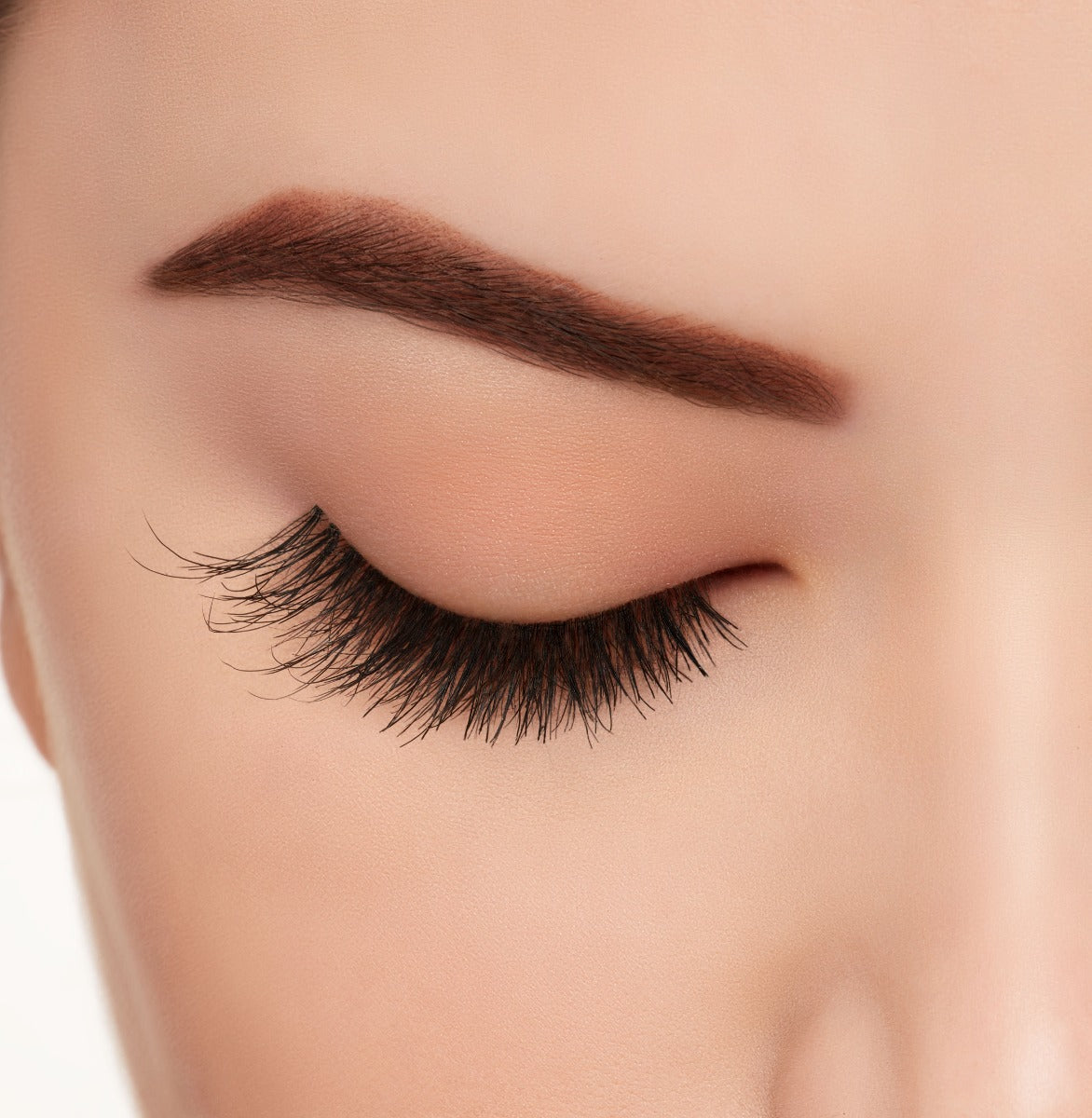 A woman wearing Ardell's Wispies 702 with a closed right eye featuring its medium-length, full volume lash effect