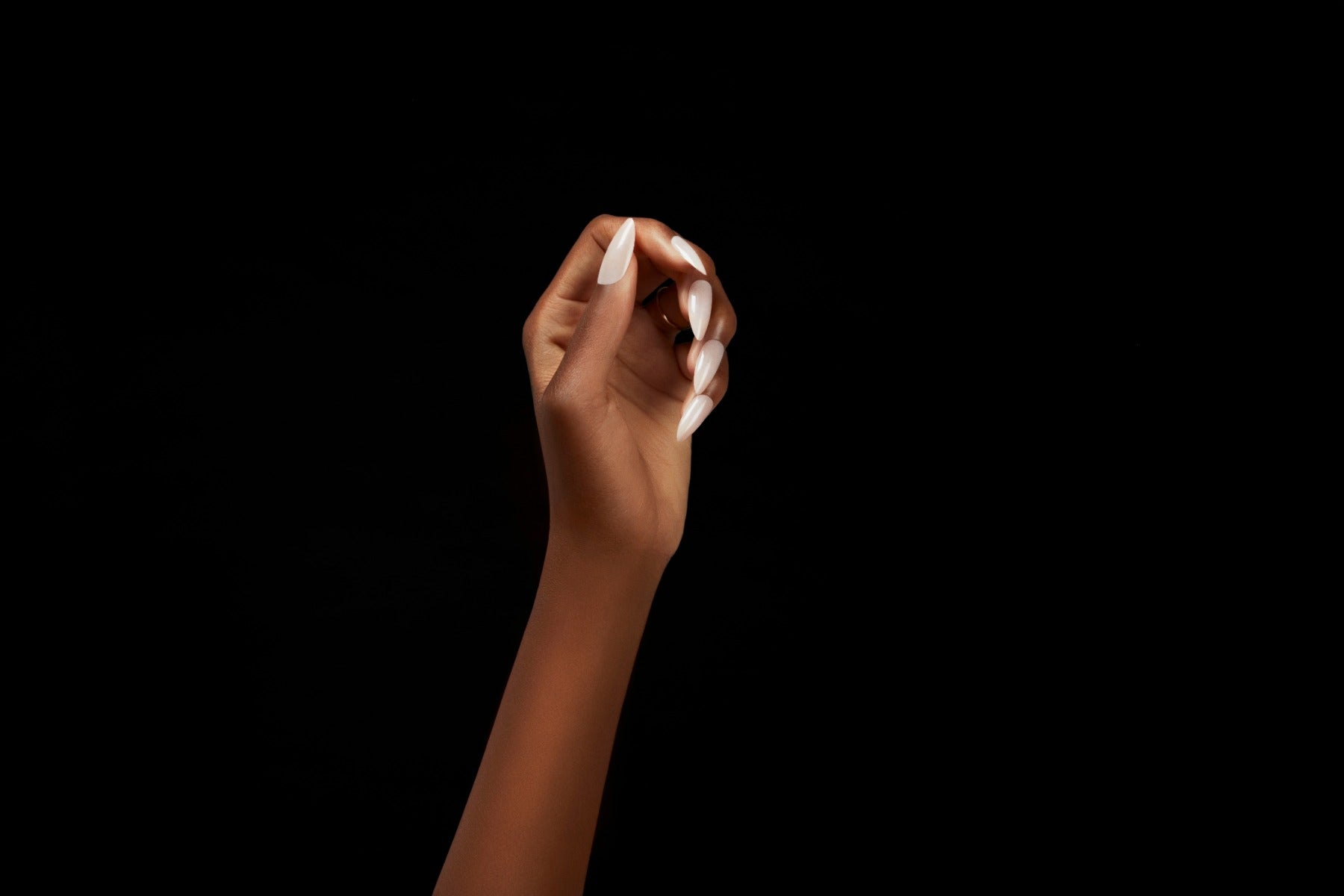 Almond-shaped press-on nails with a glossy nude base and coral French tips shown on hand.