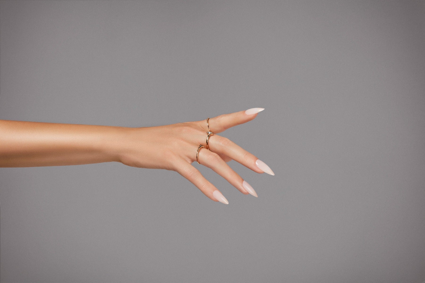 Nude and coral almond nails styled on hand, featuring minimal chic rings for added elegance.