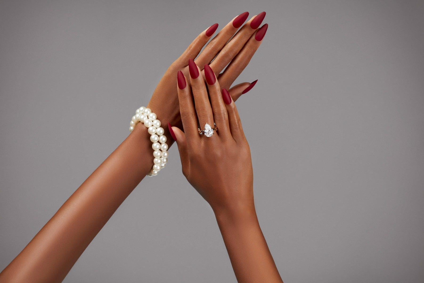 Burgundy almond nails with matte finish and pearl bracelet styled on elegant dark hands.