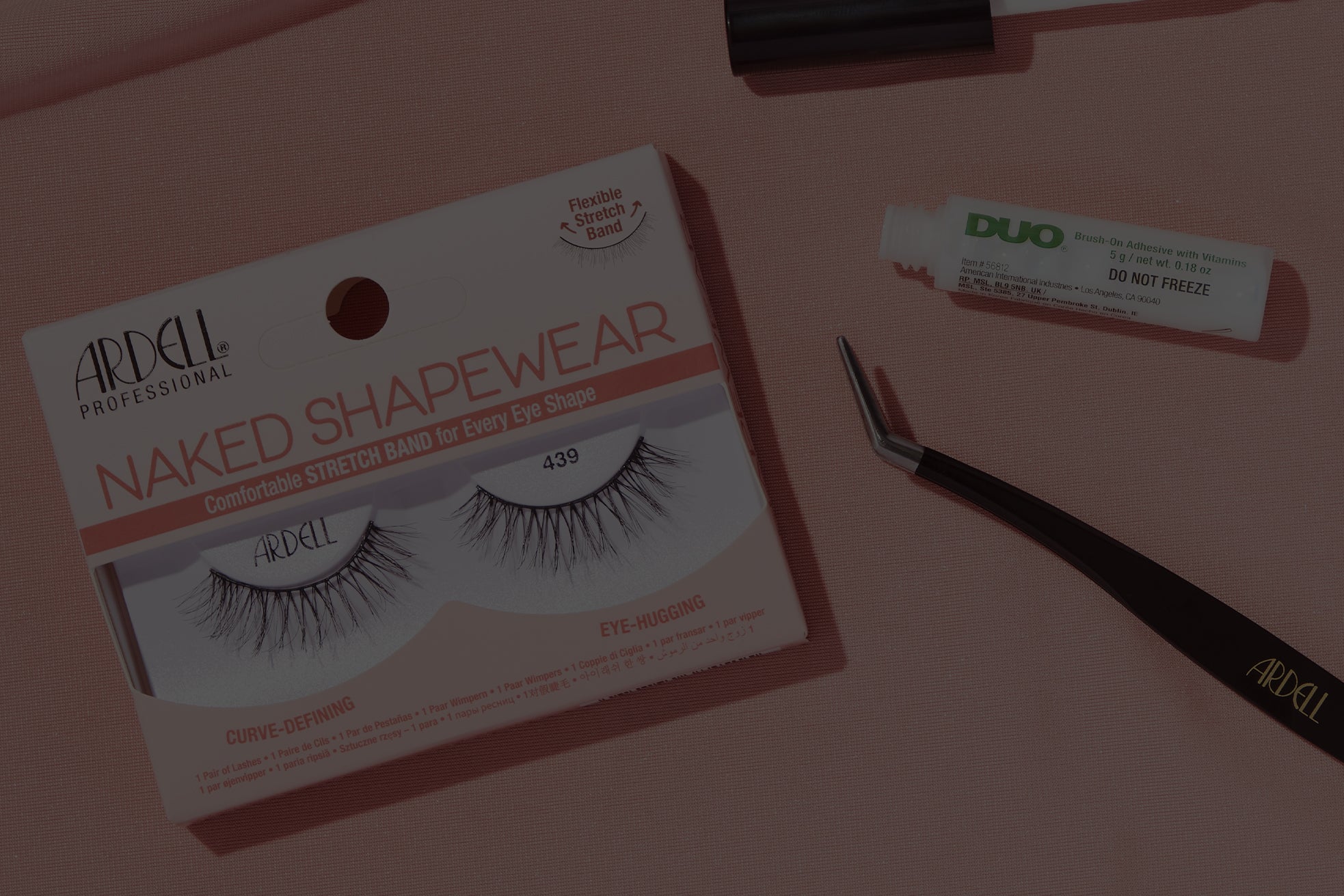 Ardell Naked Shapewear packaging, Duo glue, and twicers on a pink background.