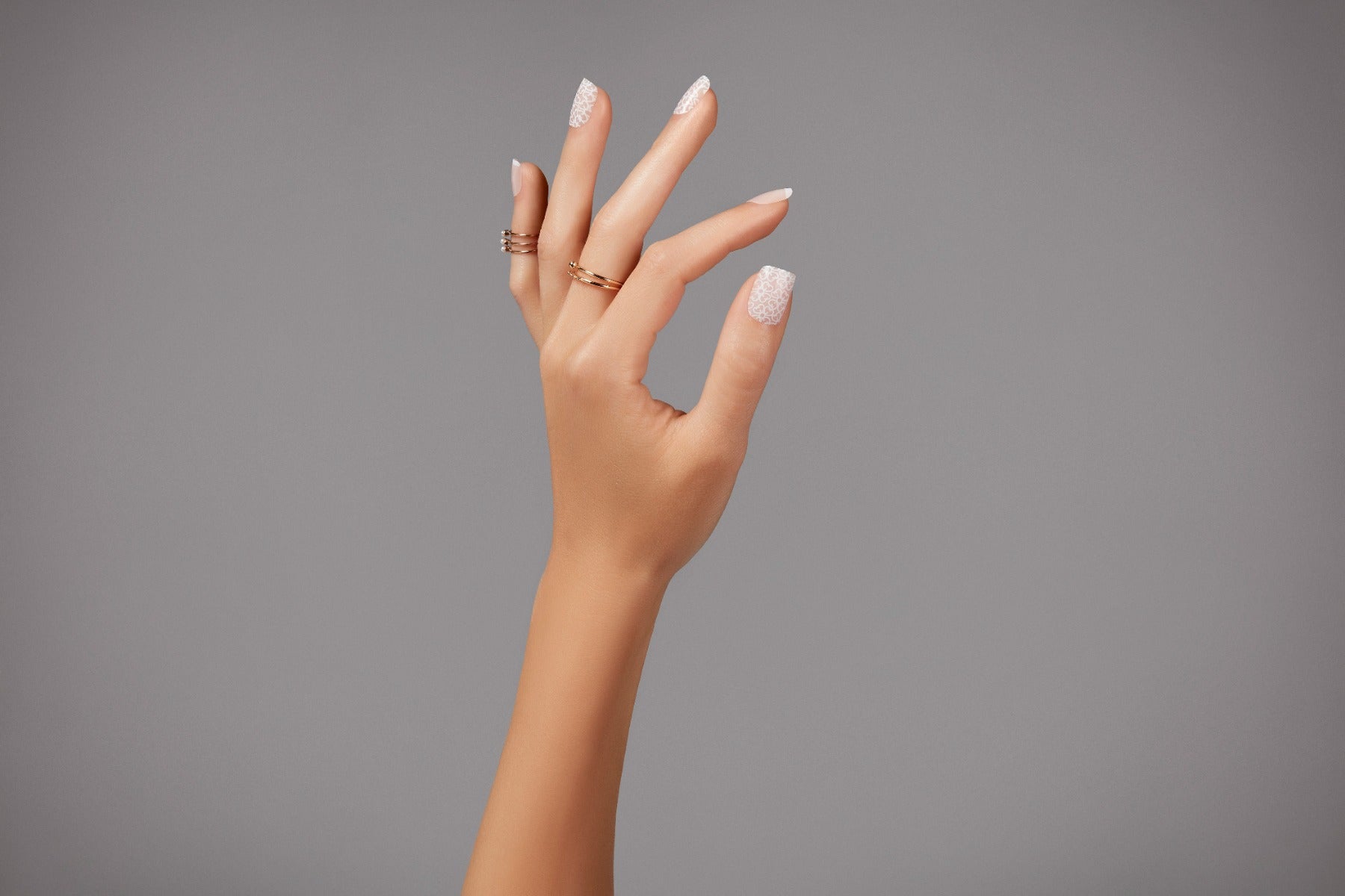 Close-up of Ardell French lace press-on nails on model’s hand, styled with gold rings for an elegant look.