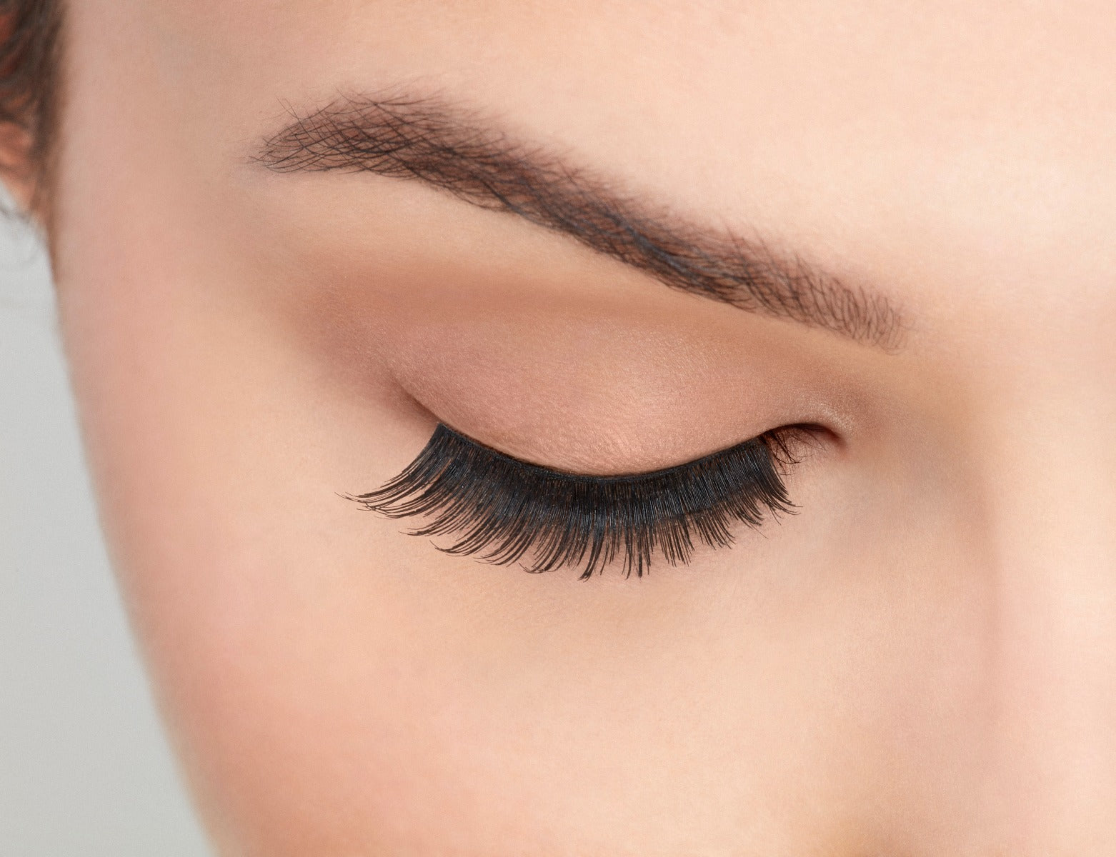 Close-up of a model's closed right eye wearing an Ardell Natural 106 false lash
