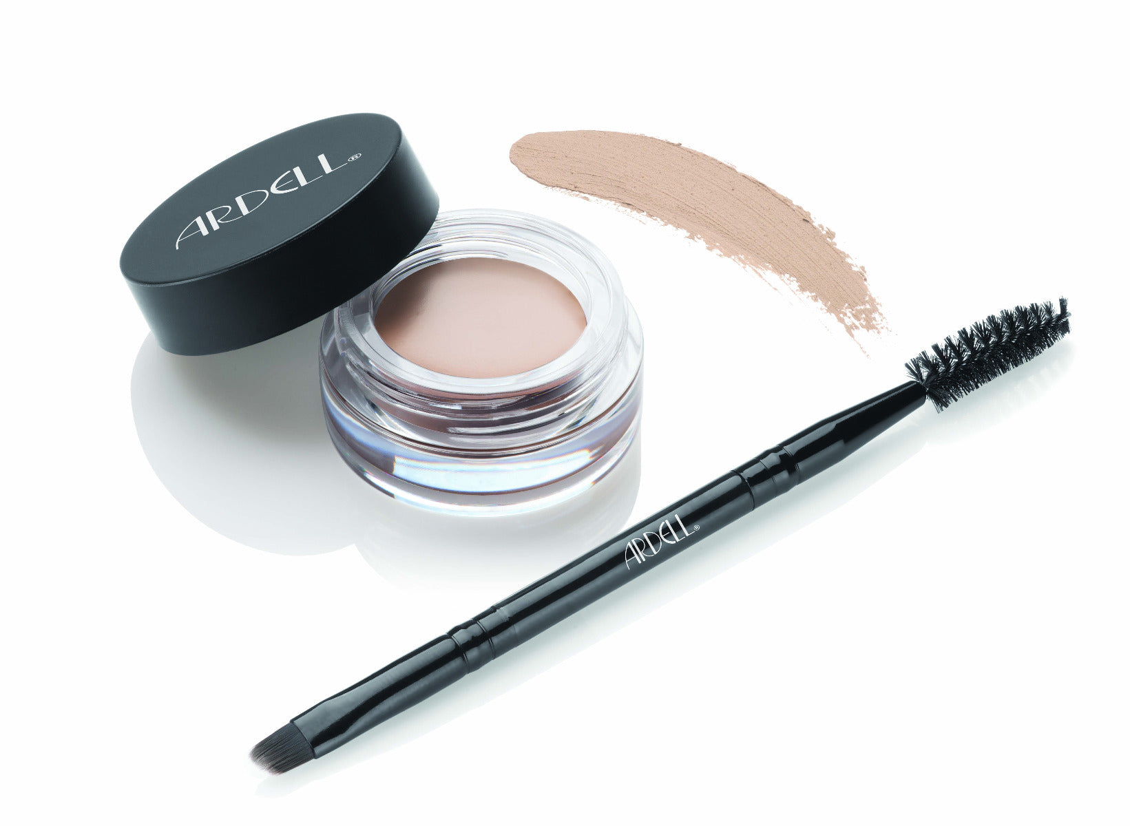 Uncapped container of Ardell Brow Pomade alongside brush/spoolie tool with pomade swatched onto background to show color