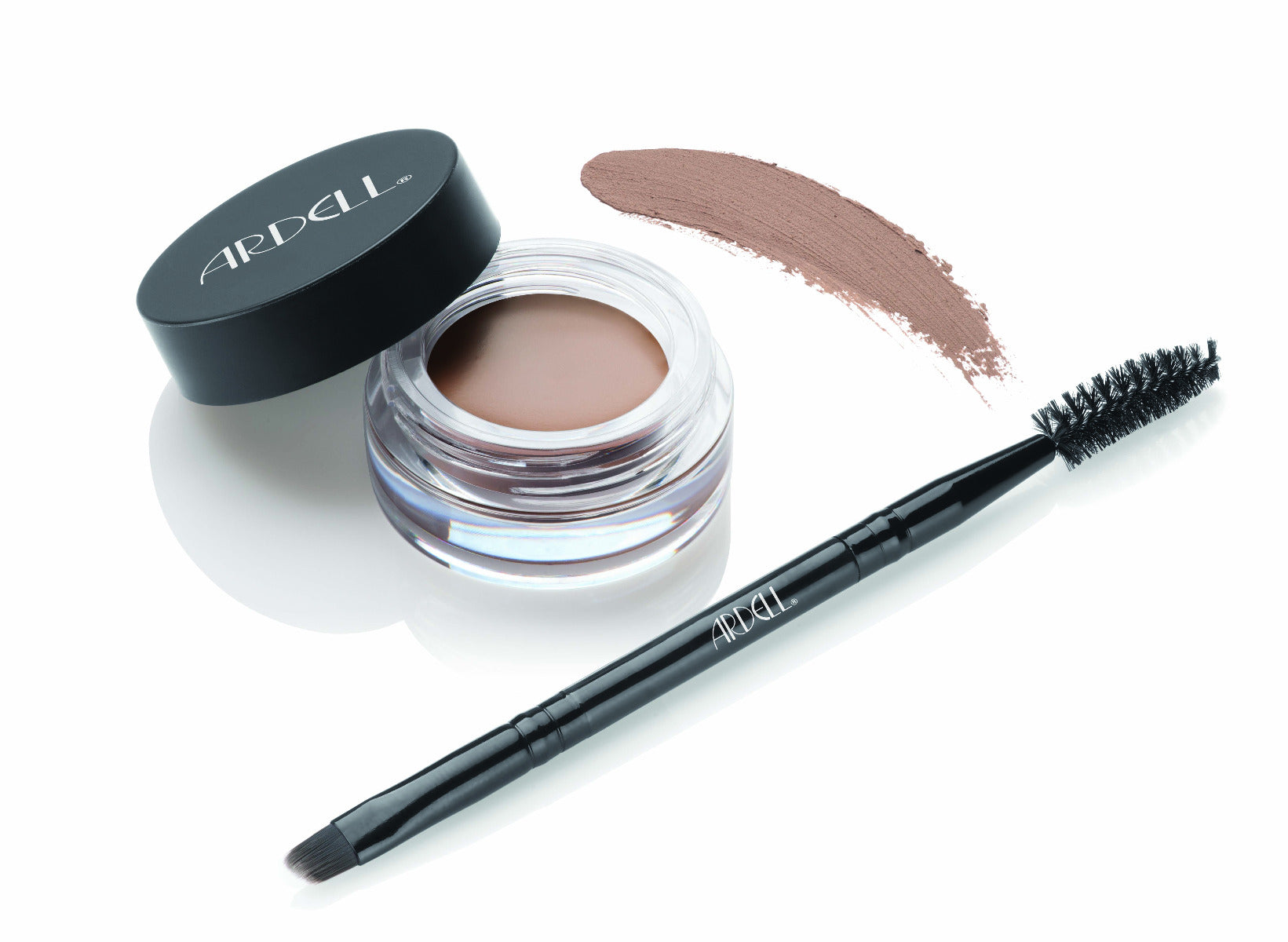 Uncapped container of Ardell Brow Pomade alongside brush/spoolie tool with pomade swatched onto the background to show color