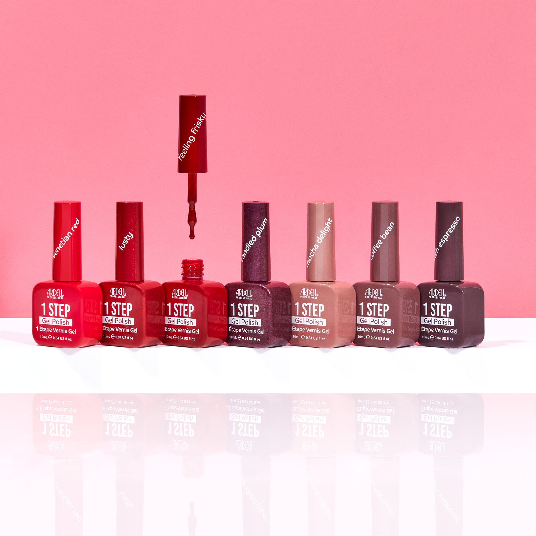 Six bottles of Maybelline New York 1 Step Nail Color in a gradient of red, burgundy, plum, nude, taupe, and brown, arranged on a reflective white surface against a solid pink background.